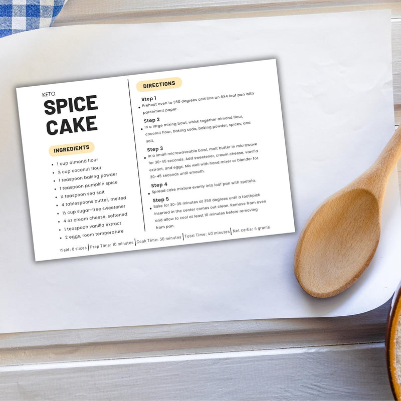 Mockup of modern keto recipe card displaying the full recipe card on parchment paper surrounded by kitchen tools and ingredients like eggs and almond flour, nearby is a kitchen towel with blue and white checkered pattern.
