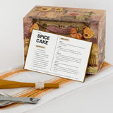 Mockup of modern keto recipe card displaying the full recipe card next to an autumn themed recipe box on a orange and white kitchen towel with measuring spoons nearby.